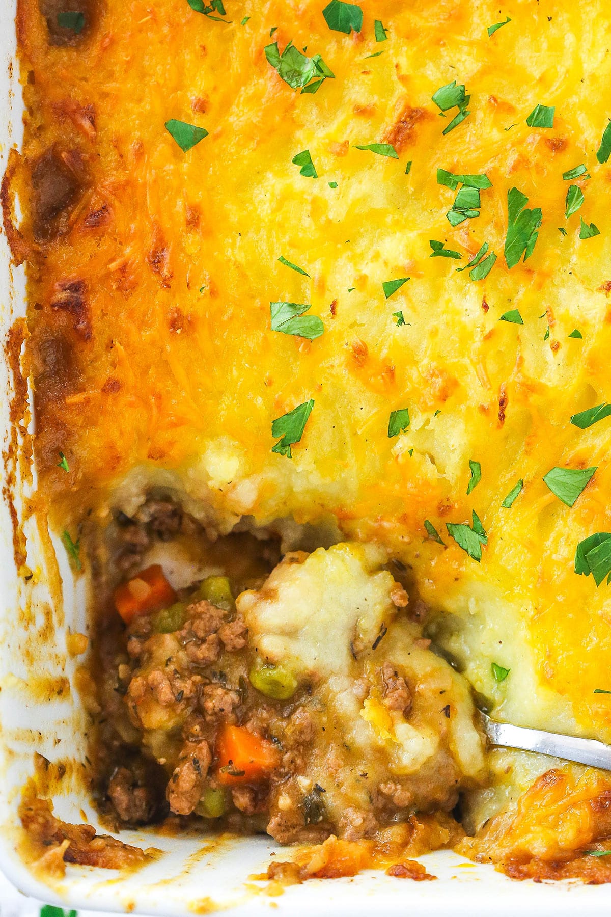 This easy Sheperd's Pie is made of perfectly seasoned ground beef and veggies topped with mashed potatoes and cheese and baked to bubbly. Shepherd's pie in a baking dish with a slice taken out of it.