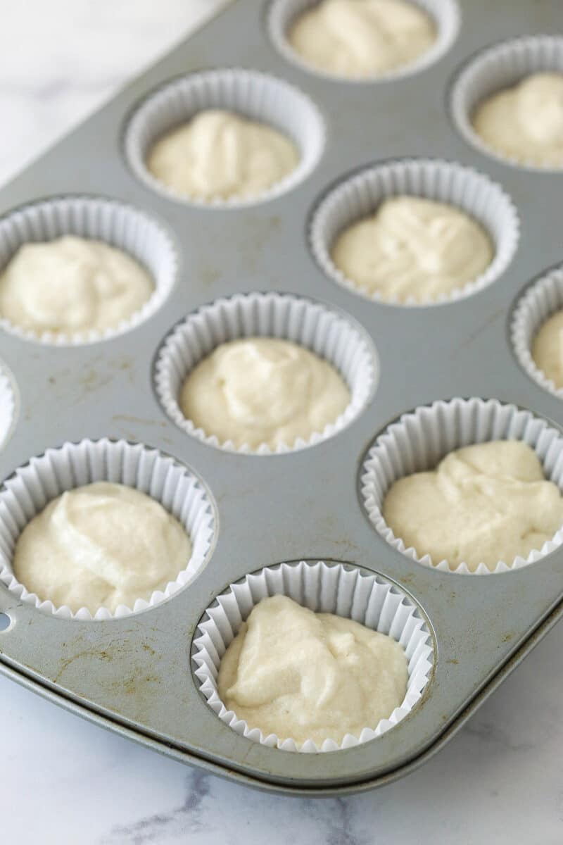 White cupcake batter in lined cupcake tins ready to be baked.