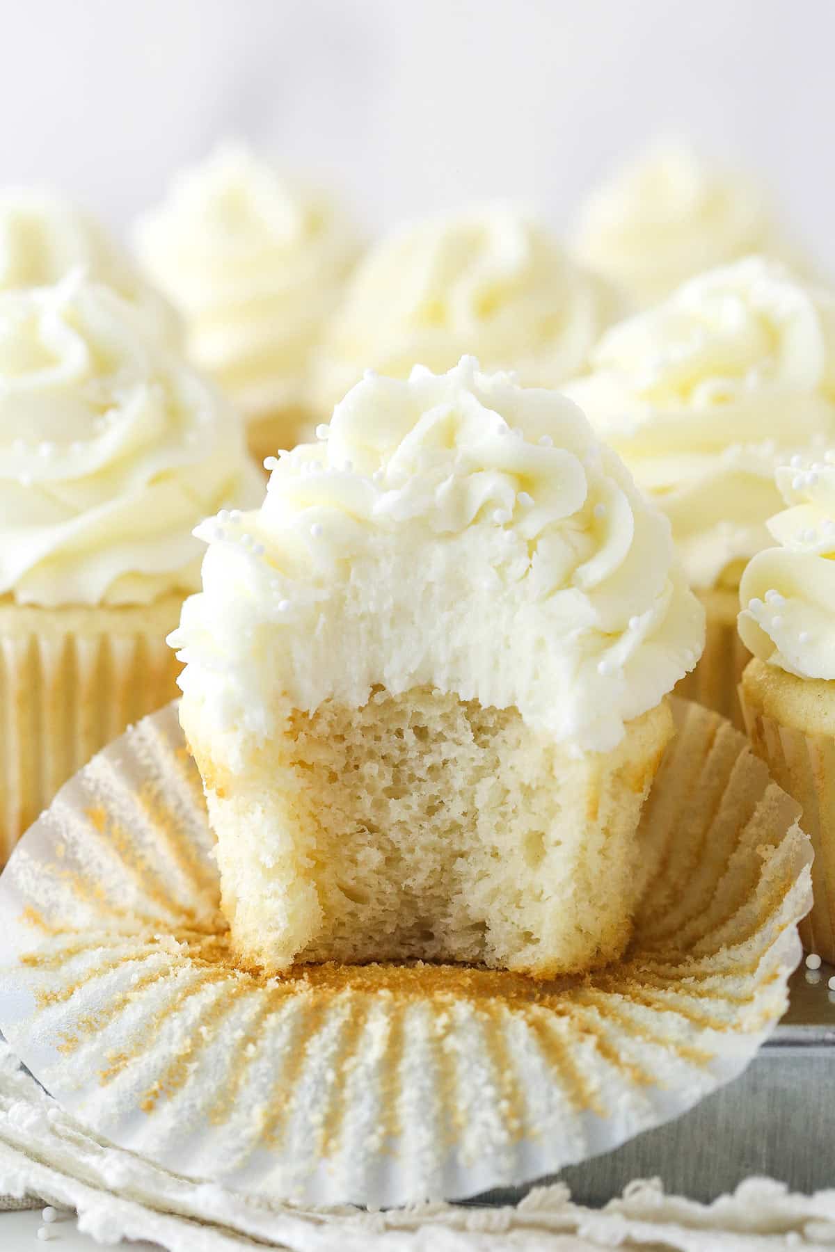 White cupcakes on a serving tray. One is half way unwrapped with a bite taken out of it.