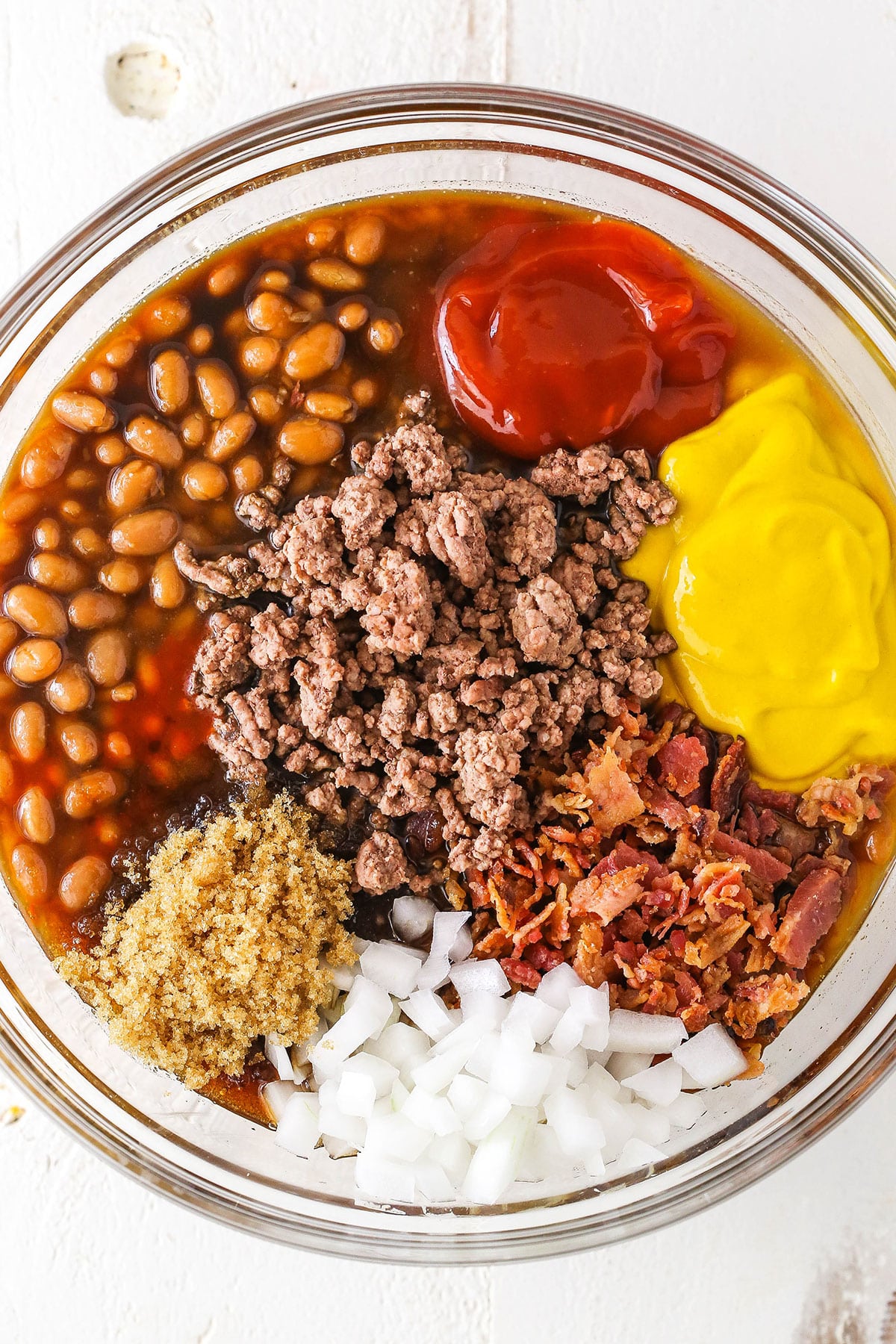 Overhead view of Mom's Amazing Baked Beans ingredients in a clear glass bowl