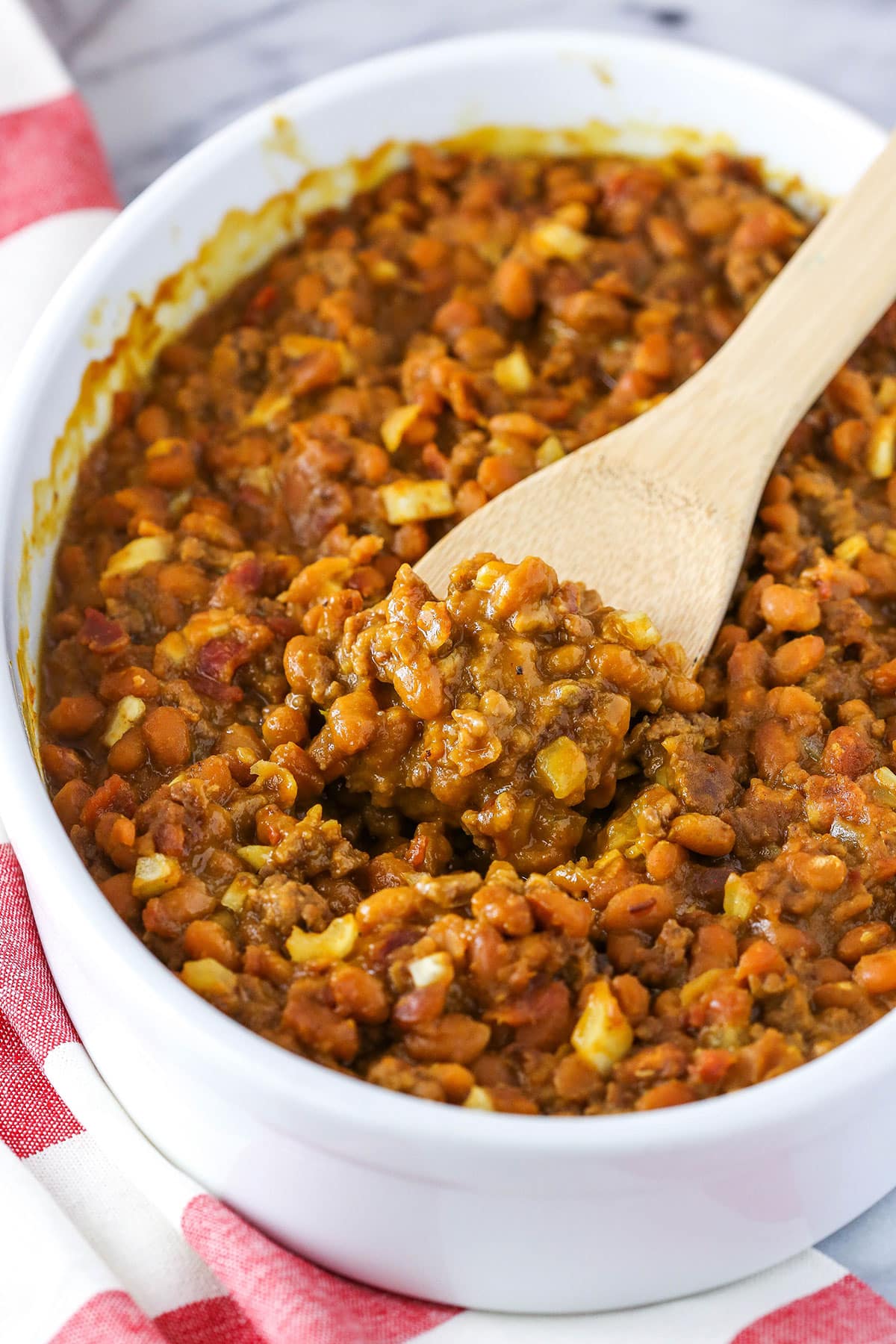 Taking a scoop of Mom's Amazing Baked Beans with a wooden spoon in a white serving dish