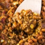 Closeup of scooping up baked beans and beef with a wooden spoon.