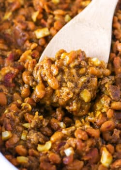 Closeup of scooping up baked beans and beef with a wooden spoon.