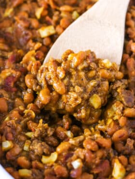 Closeup of scooping up baked beans and beef with a wooden spoon.
