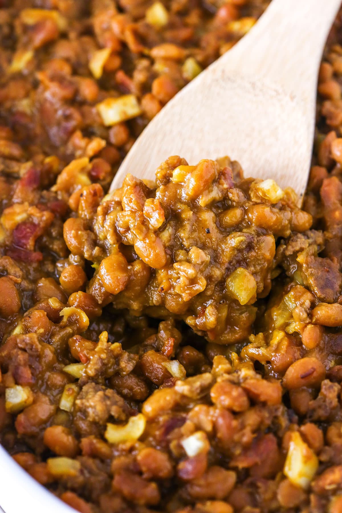 Taking a scoop of Mom's Amazing Baked Beans with a wooden spoon