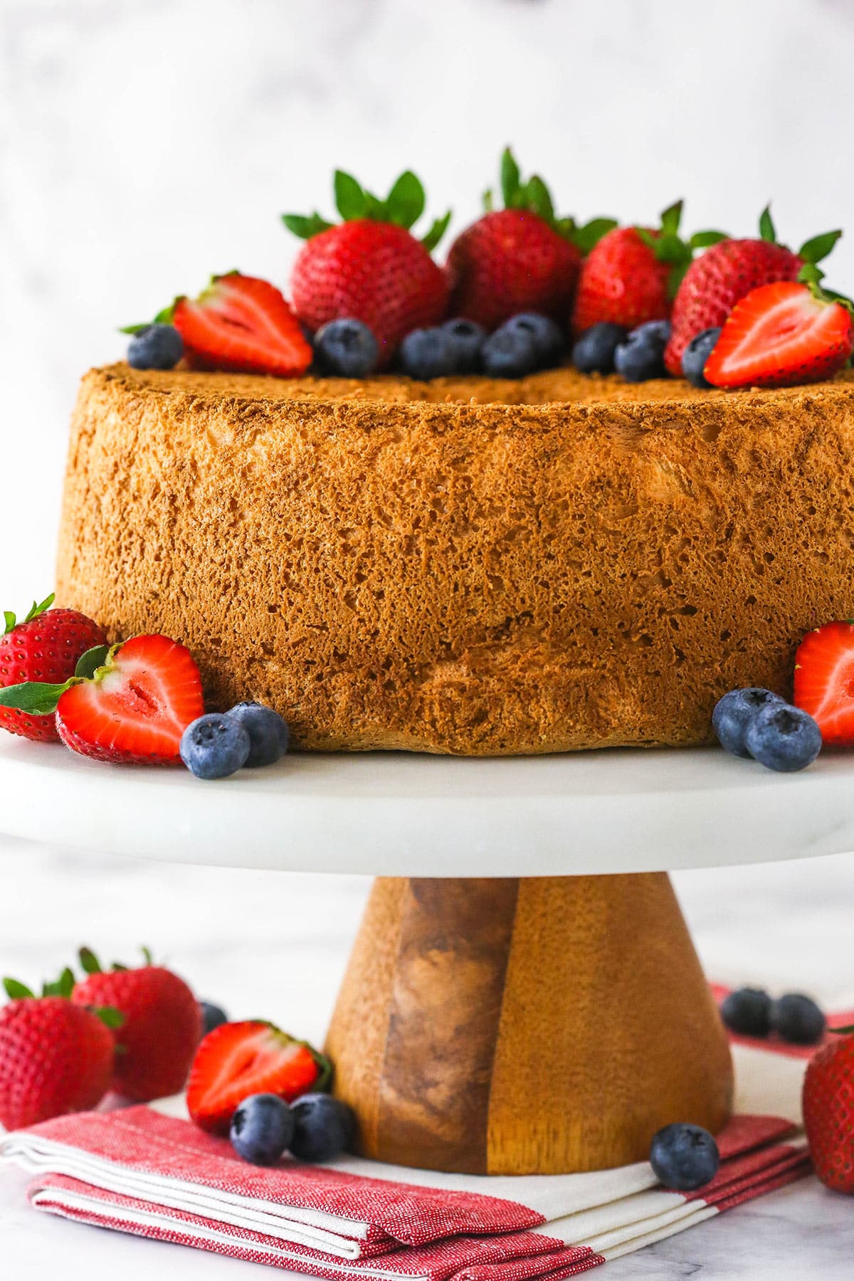 Angel food cake on a cake stand topped with and surrounded by fresh berries.