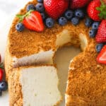 Overhead of angel food cake with a slice taken out of it topped with and surrounded by fresh berries.