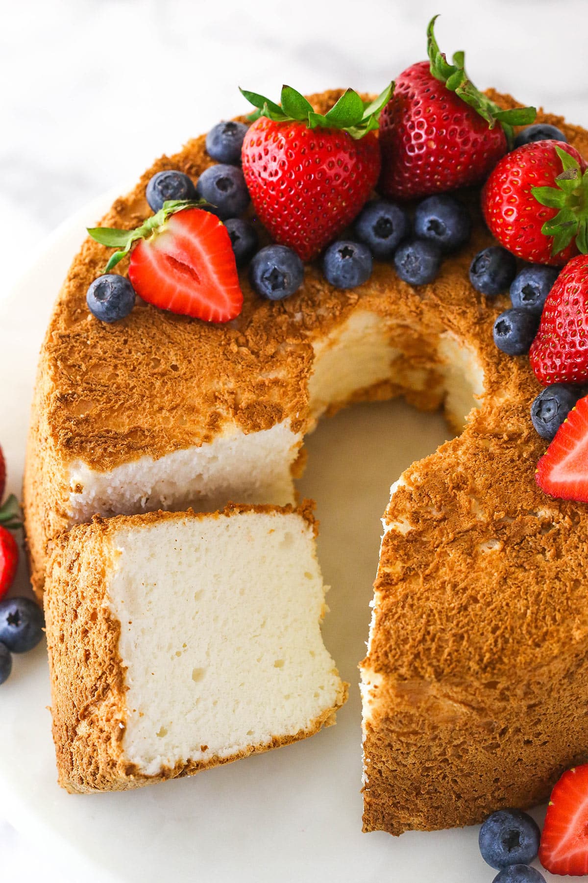 Overhead of angel food cake with a slice taken out of it topped with and surrounded by fresh berries.