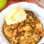 A single serving of Apple Crisp with a scoop of vanilla ice cream in a white bowl with a spoon