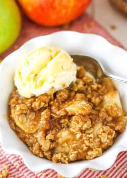 A single serving of Apple Crisp with a scoop of vanilla ice cream in a white bowl with a spoon