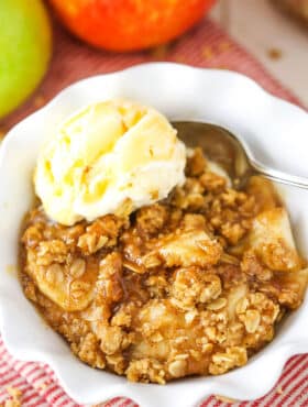 A single serving of Apple Crisp with a scoop of vanilla ice cream in a white bowl with a spoon