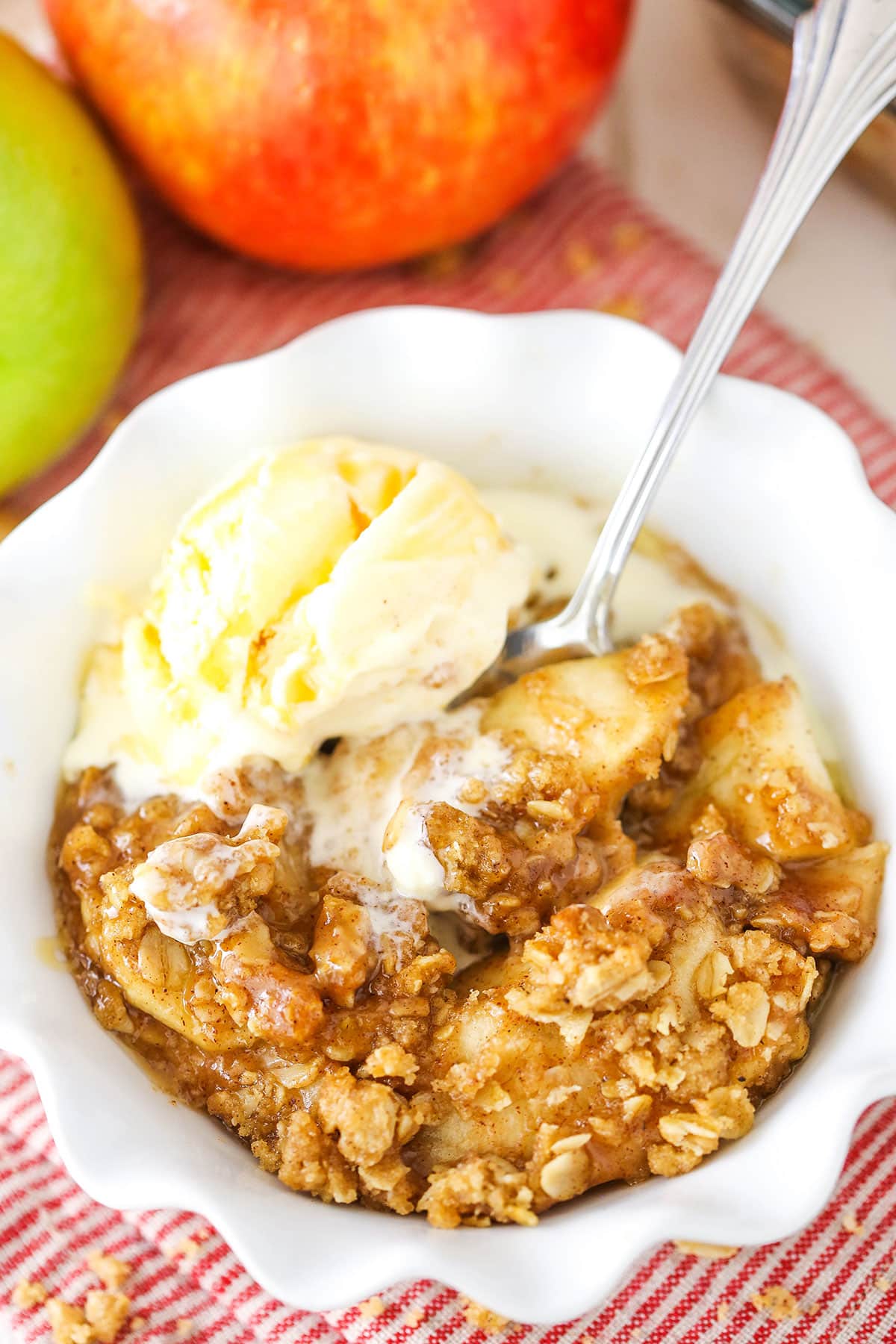 A single serving of Apple Crisp with a scoop of vanilla ice cream in a white bowl with a spoon