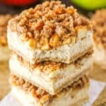 An Apple Streusel Cheesecake Bar with a bite removed stacked on top of two more Apple Streusel Cheesecake Bars