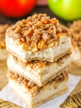 An Apple Streusel Cheesecake Bar with a bite removed stacked on top of two more Apple Streusel Cheesecake Bars