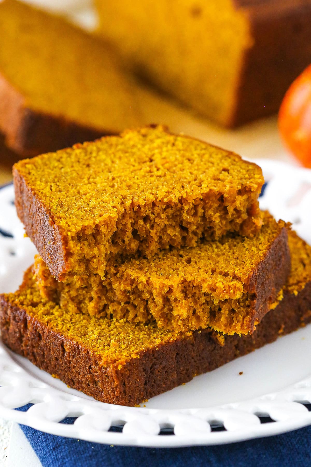 This easy pumpkin bread recipe makes 2 soft, moist loaves with the perfect amount of that classic pumpkin spice flavor you know and love. Two halves of Pumpkin Bread on top of another slice of Pumpkin Bread on a white plate