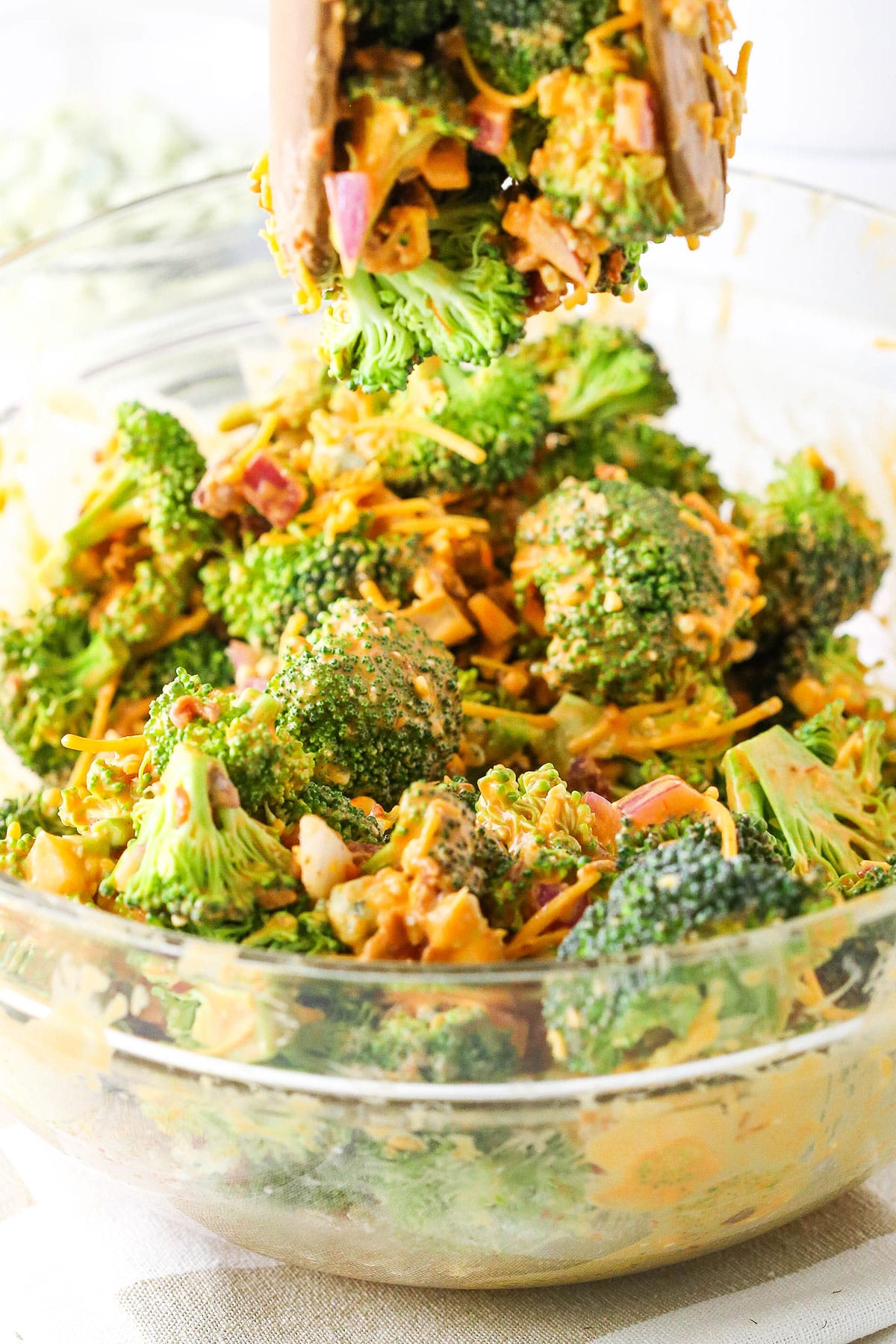 Buffalo Broccoli Salad ingredients being mixed together in a clear glass bowl