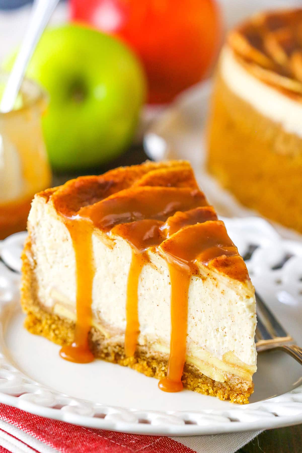 A slice of Caramel Apple Cheesecake next to a fork on a white plate