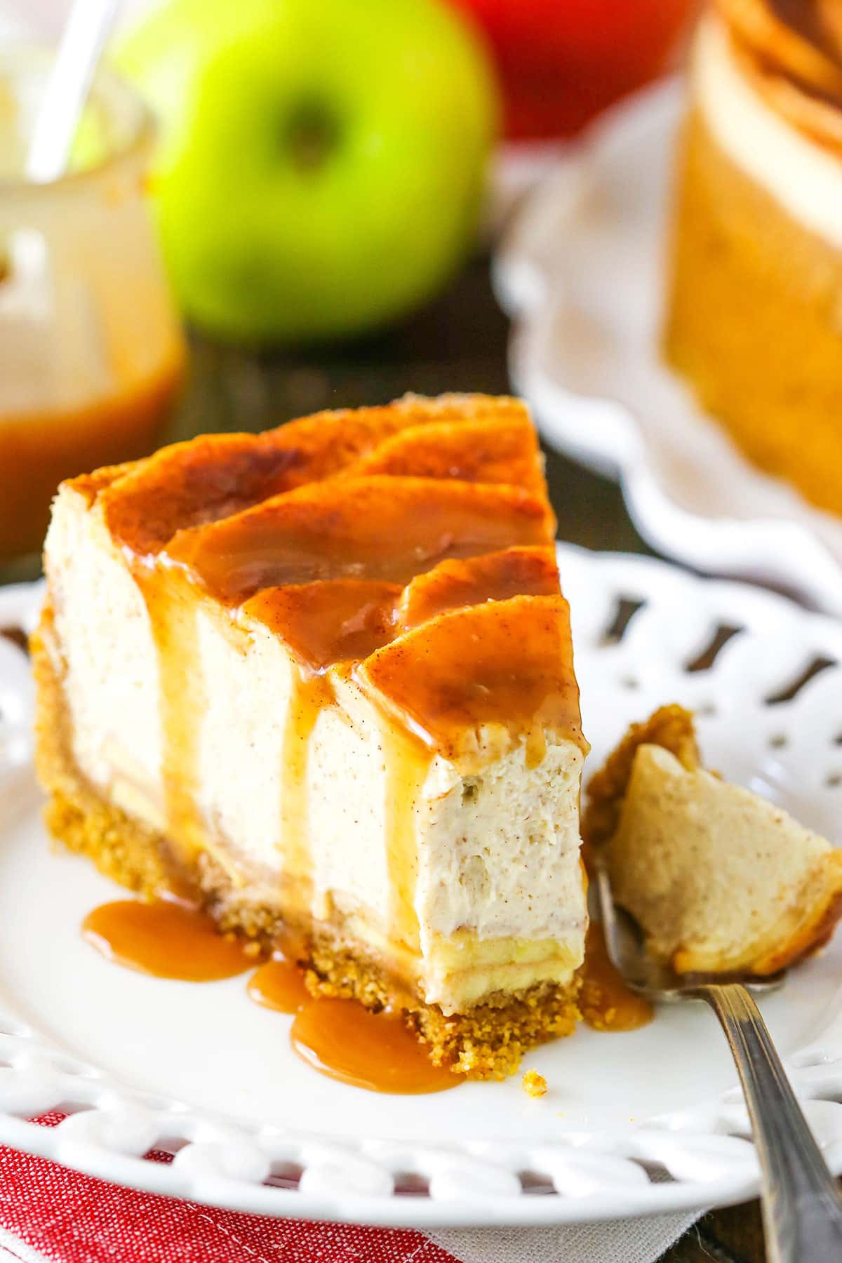 A slice of Caramel Apple Cheesecake with a bite removed next to a fork on a white plate