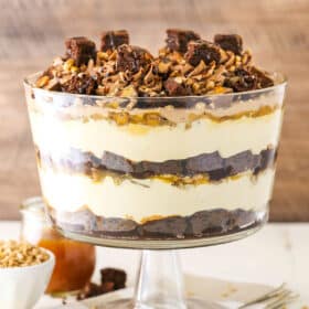 Side view of Caramel Cheesecake Brownie Trifle in a clear glass cake stand