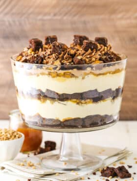 Side view of Caramel Cheesecake Brownie Trifle in a clear glass cake stand
