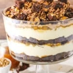 Side view of Caramel Cheesecake Brownie Trifle in a clear glass cake stand