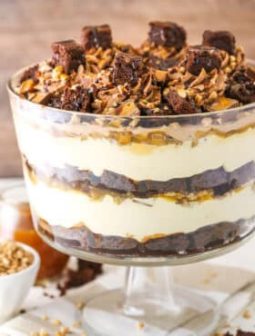 Side view of Caramel Cheesecake Brownie Trifle in a clear glass cake stand