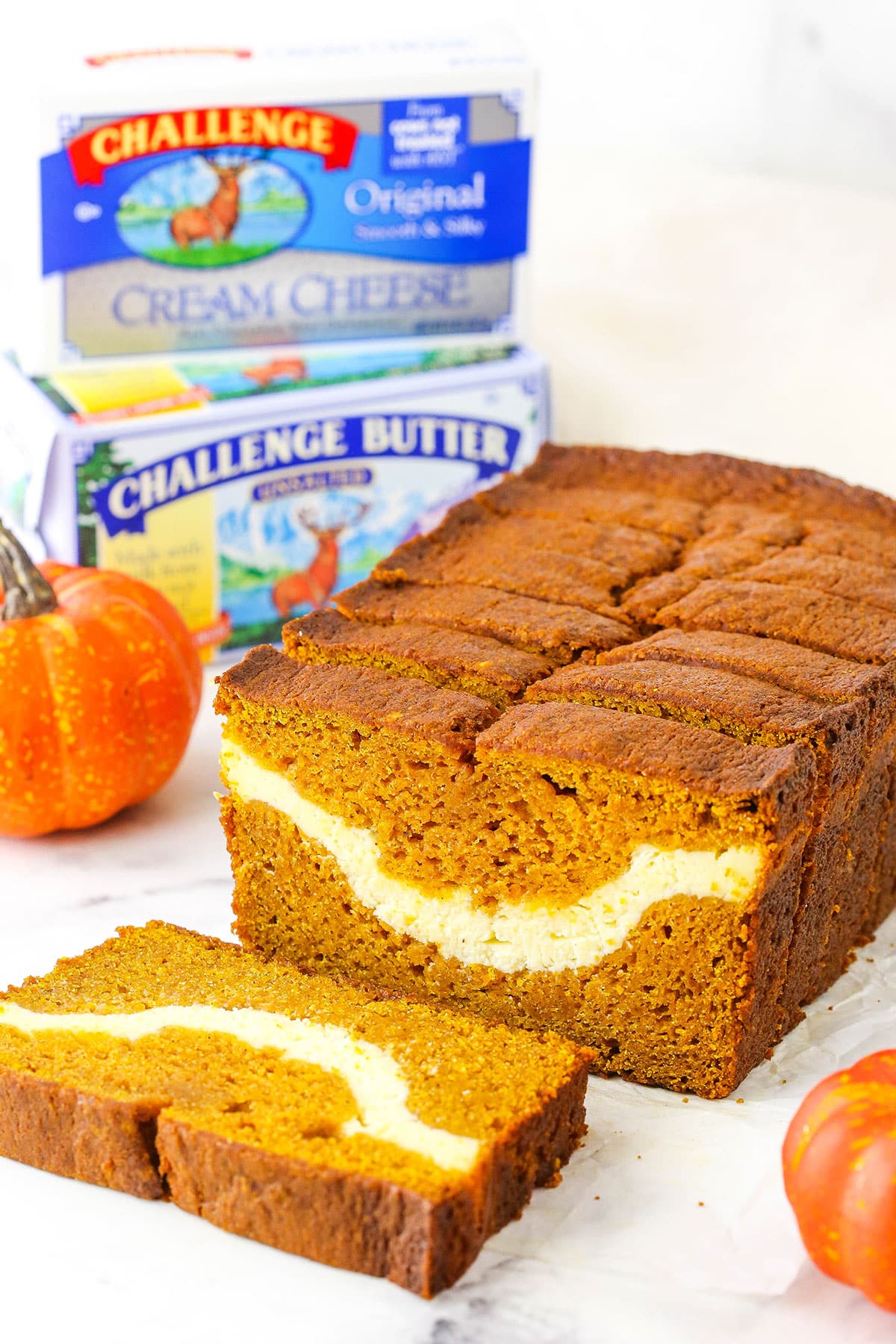 Side view of Cheesecake Swirl Pumpkin Bread sliced with the front slice removed and Challenge Butter in the background