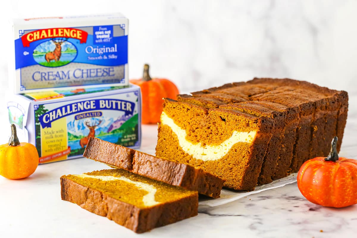 Side view of Cheesecake Swirl Pumpkin Bread sliced with the front two slices facing up and Challenge Butter in the background