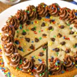 A full Chocolate Chip Cookie Cake with a slice cut out on a white plate