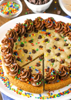 A full Chocolate Chip Cookie Cake with a slice cut out on a white plate