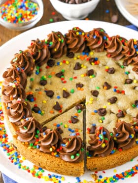 A full Chocolate Chip Cookie Cake with a slice cut out on a white plate