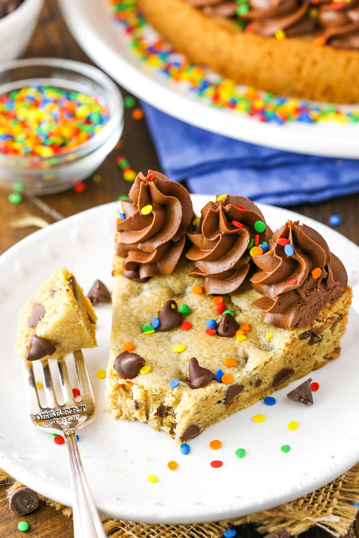 A slice of Chocolate Chip Cookie Cake with a bite removed on a white plate