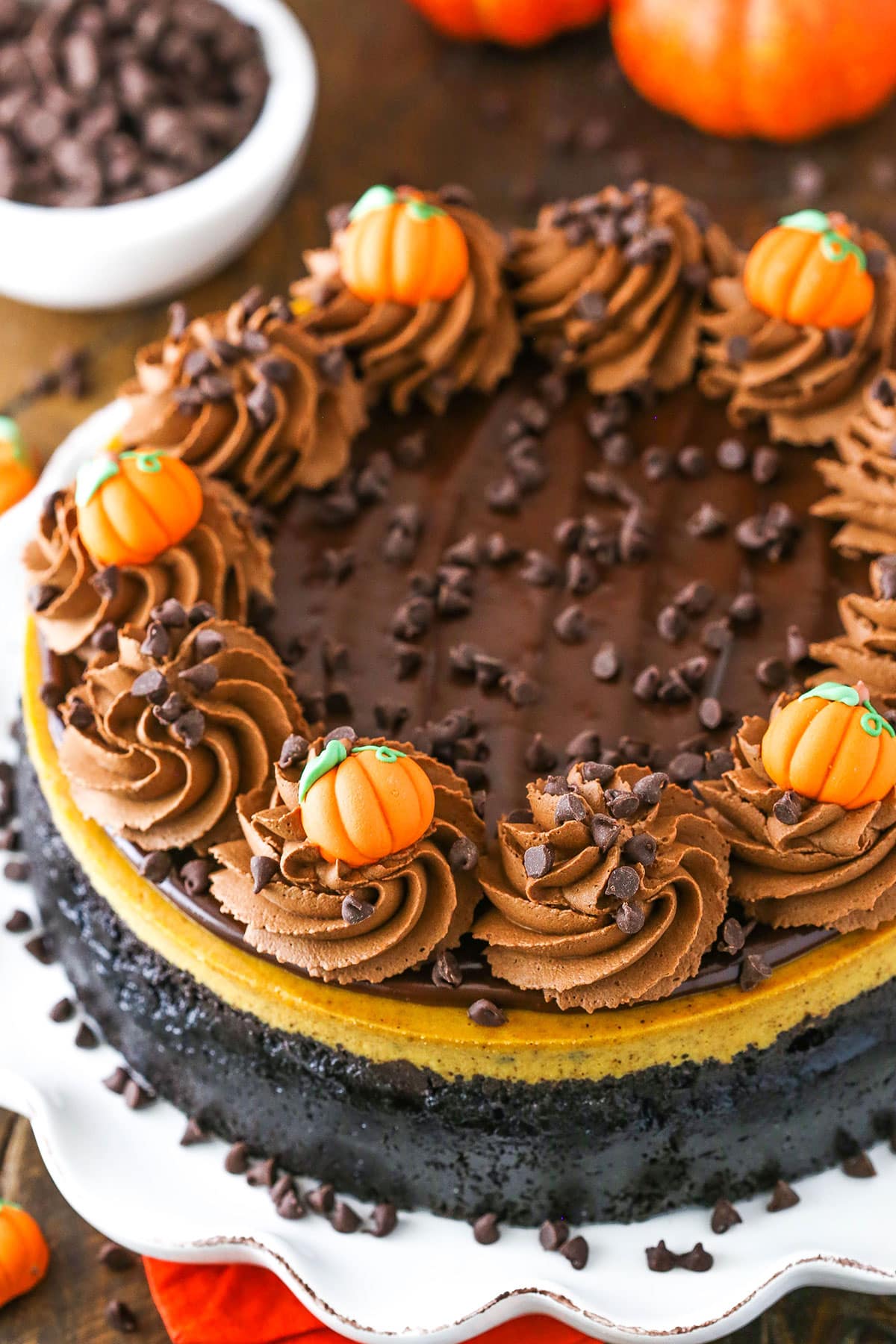 Overhead view of a full Chocolate Chip Pumpkin Cheesecake topped with chocolate swirls and candy pumpkins on a white serving platter