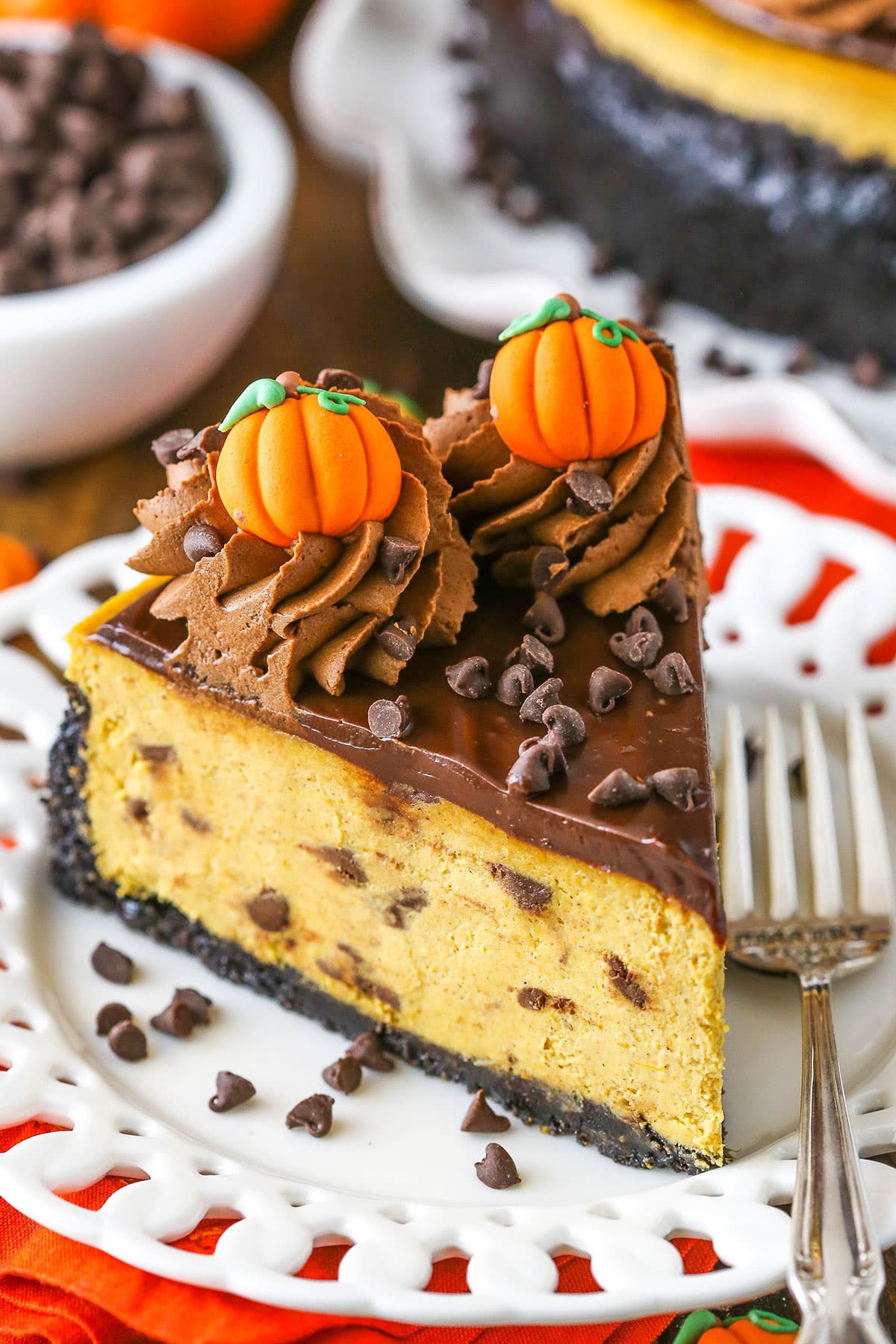 This Chocolate Chip Pumpkin Cheesecake is thick, creamy and full of pumpkin and chocolate! It's a great flavor combination and such a fun Thanksgiving dessert idea! A slice of Chocolate Chip Pumpkin Cheesecake next to a silver fork on a white plate