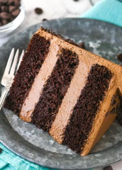 A slice of chocolate mousse cake on a plate with a fork near a bowl of chocolate chips.