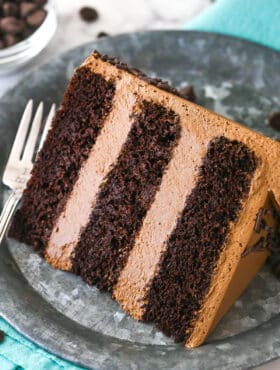 A slice of chocolate mousse cake on a plate with a fork near a bowl of chocolate chips.