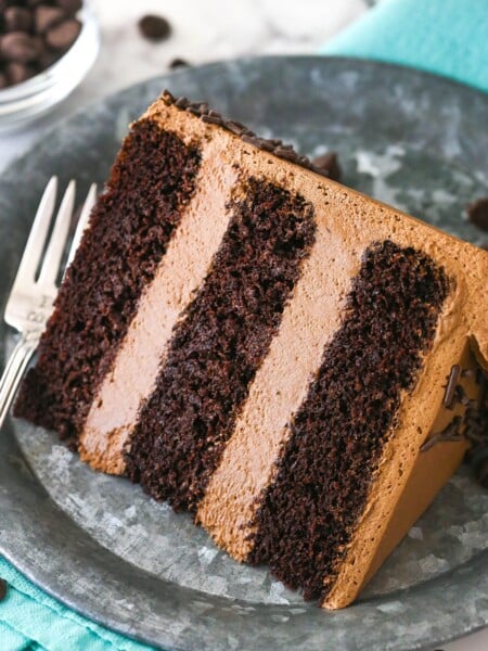 A slice of chocolate mousse cake on a plate with a fork near a bowl of chocolate chips.