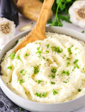 A bowl of garlic mashed potatoes garnished with fresh parsley and freshly cracked black pepper.