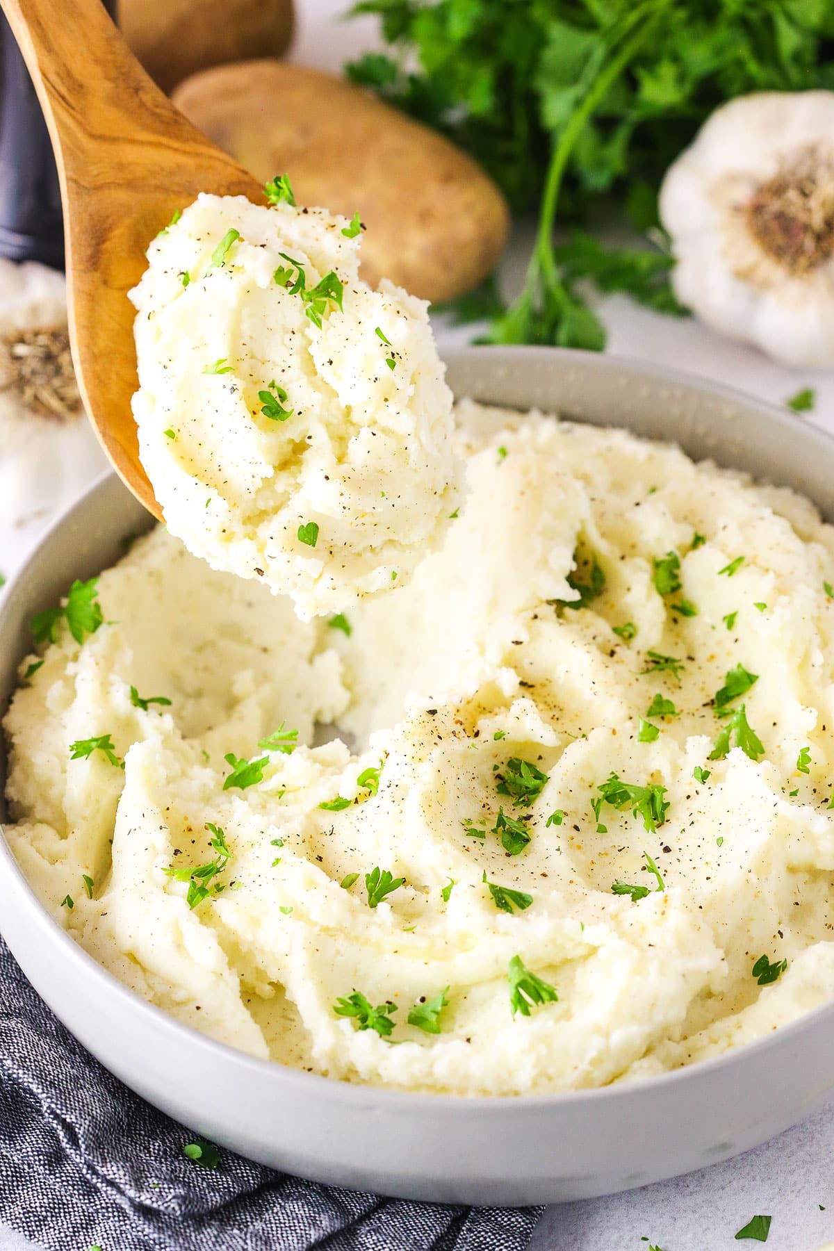 Chunky Garlic Mashed Potatoes in a white bowl with a wooden spoon scooping a serving