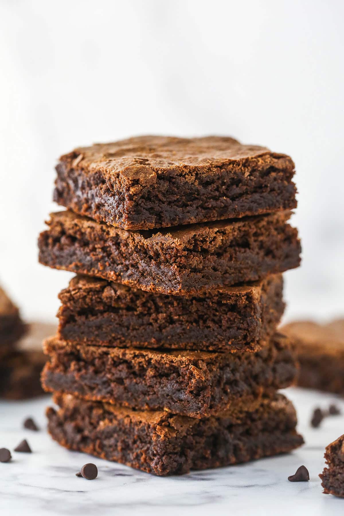 A stack of homemade brownies surrounded by chocolate chips.