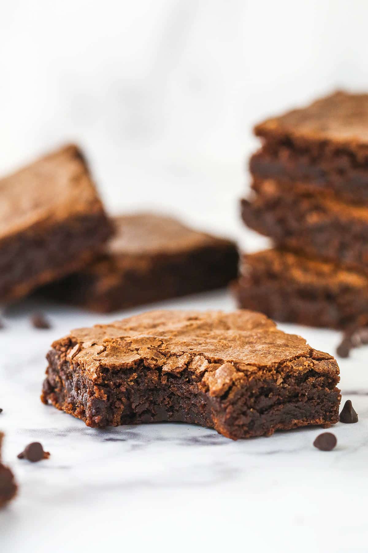 Closeup of a brownie with a bight out of it. There are more brownies stacked behind it.