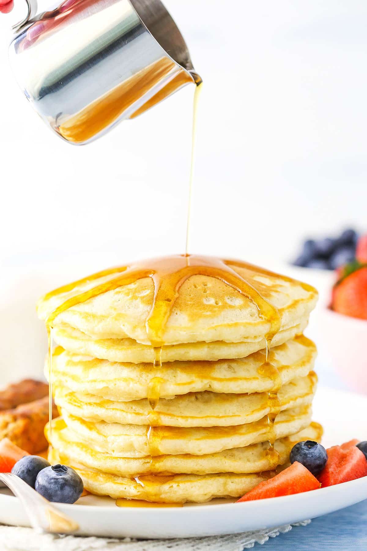 Pouring syrup over Seven Fluffy Homemade Pancakes stacked on a white plate