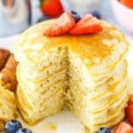 Fluffy Homemade Pancakes stacked with a quarter removed on a white plate