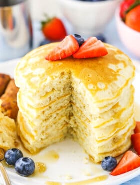 Fluffy Homemade Pancakes stacked with a quarter removed on a white plate