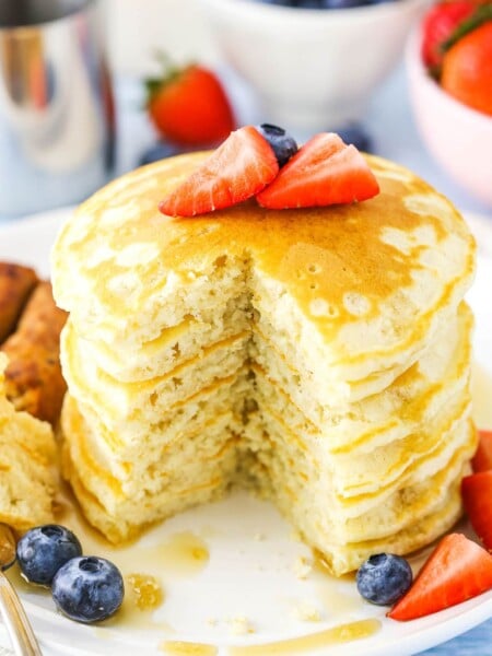 Fluffy Homemade Pancakes stacked with a quarter removed on a white plate