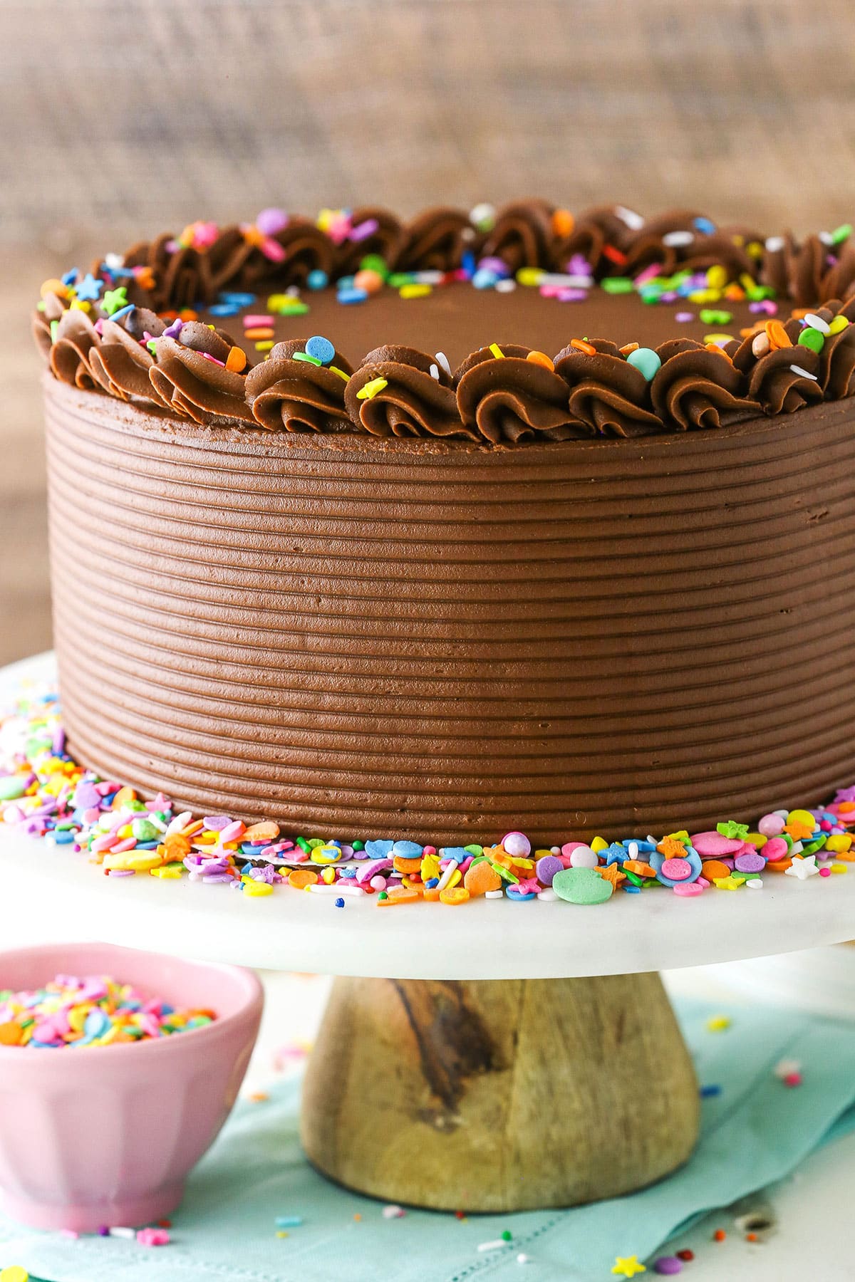 Side view of Yellow Cake with Chocolate Frosting and colorful sprinkles on a white cake stand