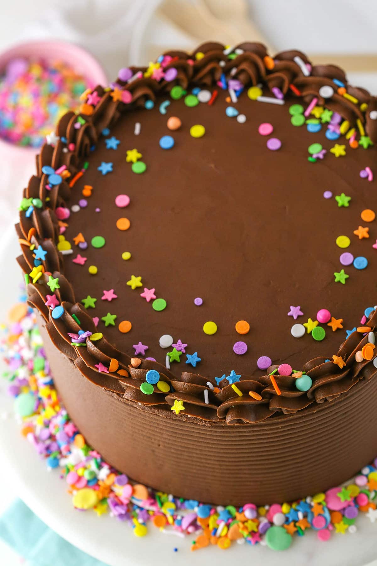 Overhead view of Yellow Cake with Chocolate Frosting and colorful sprinkles on a white cake stand