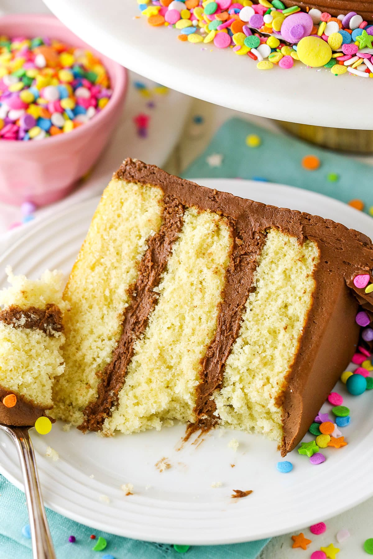 A slice of Yellow Cake with a bite removed next to a fork on a white plate