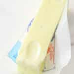 stick of softened butter partially unwrapped on marble background with a fingerprint