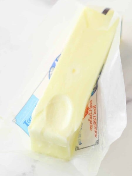 stick of softened butter partially unwrapped on marble background with a fingerprint